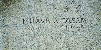 A photograph of engraved stone reading “I HAVE A DREAM – Martin Luther King Jr.”, referencing the March on Washington for Jobs and Freedom on August 28, 1963. The image is framed from above, with a pair of black-and-white sneakers visible at the bottom edge, creating a reflective, symbolic perspective on the historic inscription.